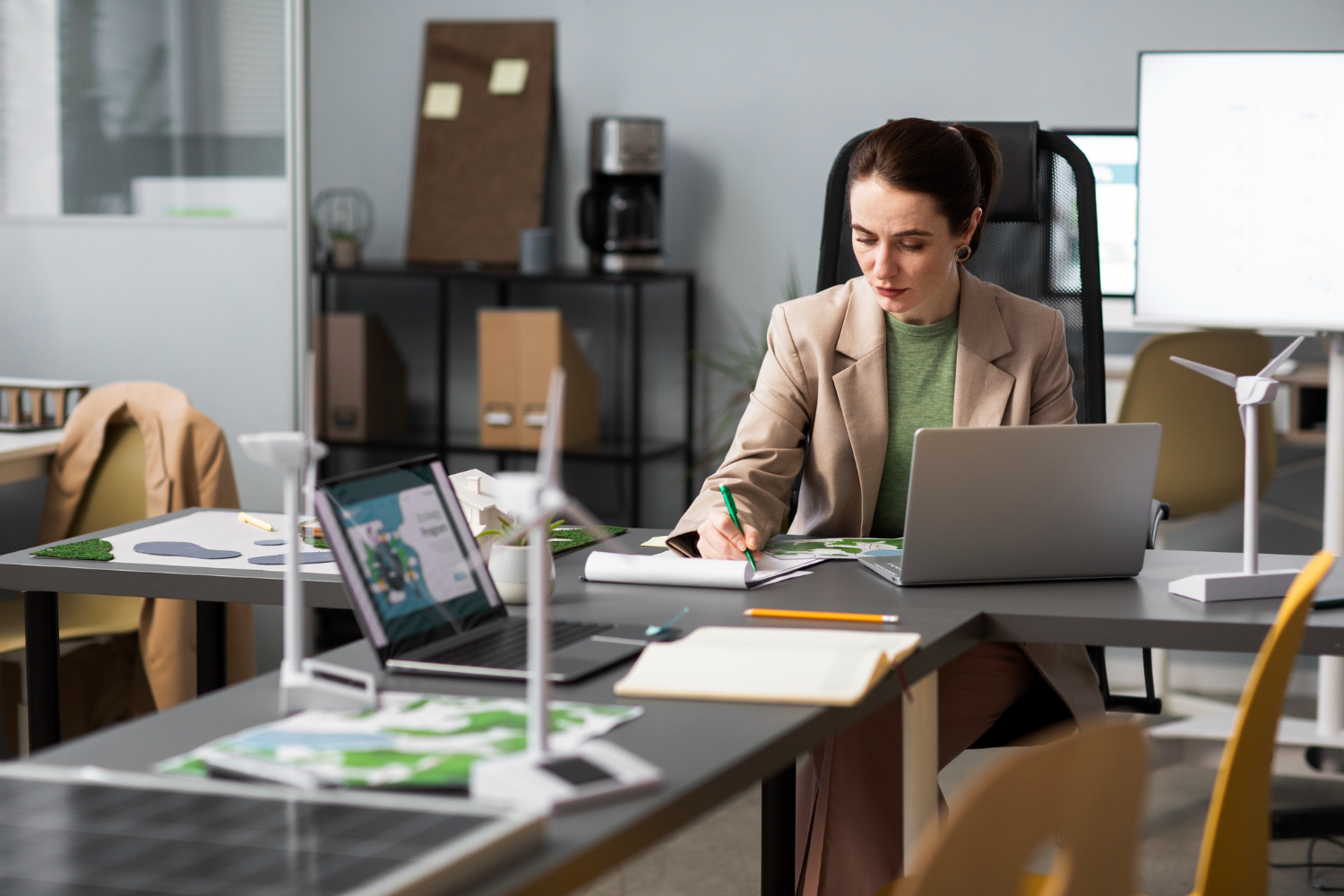 Mujer profesional trabajando en una oficina moderna con un ordenador portátil, enfocada en tareas de gestión y planificación digital.